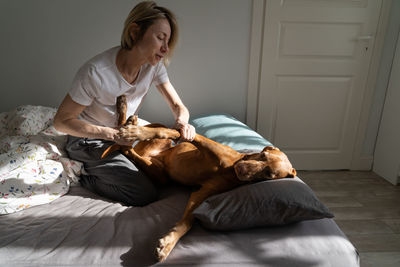 Relaxed positive girl playing with dog vizsla sits on bed in bedroom enjoy communicating with pet