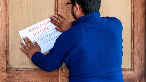Midsection of man holding paper while standing against blue wall