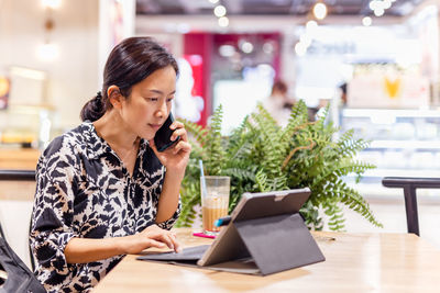 Young woman using mobile phone while sitting on table