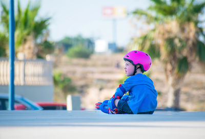 Side view of boy sitting against blue wall