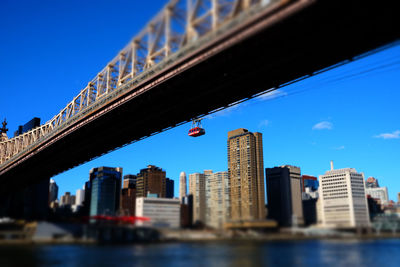 Low angle view of bridge over river by buildings against blue sky