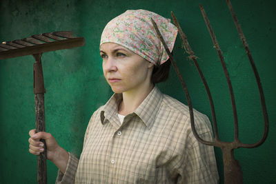 Woman holding gardening equipment while standing against wall