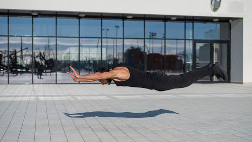 A man in black sportswear jumps while doing push-ups outdoors.