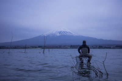 Rear view of man standing in sea against sky during sunset