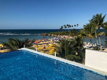 Swimming pool by sea against clear blue sky
