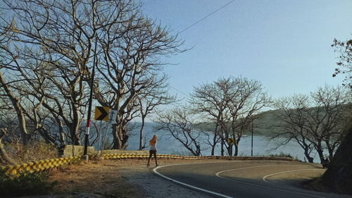 Man walking on road against bare trees