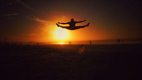 Silhouette man flying over beach against sky during sunset