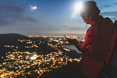 Mature man using smart phone with illuminated city against sky at night