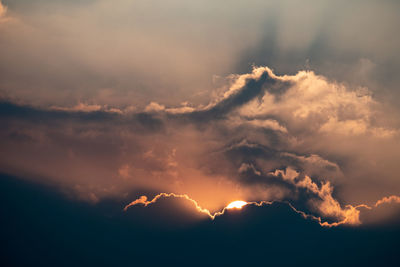 Low angle view of sun streaming through clouds during sunset