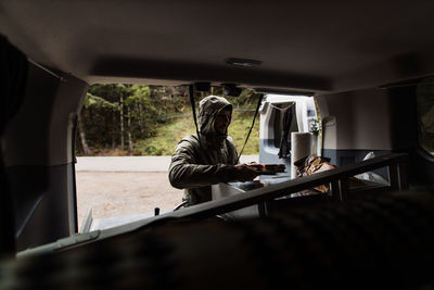 Serious male explorer standing near van and preparing food for lunch while traveling around america in autumn