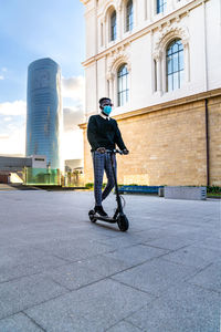 Rear view of man skateboarding on street against buildings in city