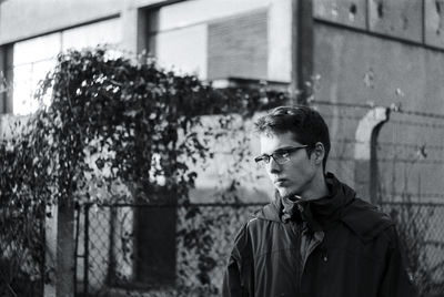 Young man wearing eyeglasses looking away while standing against building