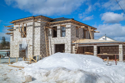 Snow covered houses by building against sky