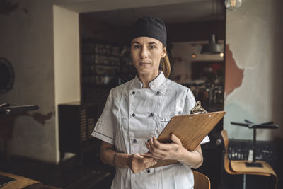 Portrait of chef with clipboard standing in restaurant