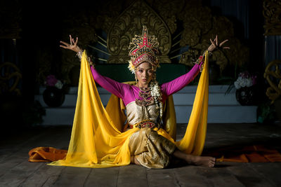 Portrait of woman in traditional clothing sitting against decoration