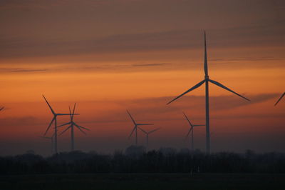 Silhouette wind turbine on field against sky during sunset