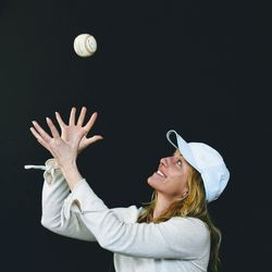 Close-up of woman catching baseball against black background