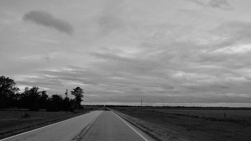 Empty road amidst field against sky