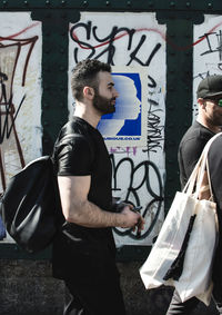 Side view of young man standing against graffiti in city