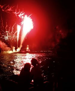 Firework display over sea against sky at night