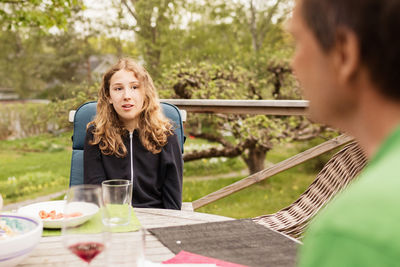 Teenage girl talking to father at table in yard