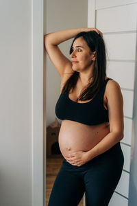 Happy pregnant woman stands at home.