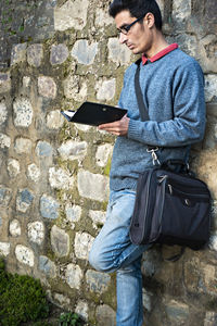 Side view of young man using mobile phone against wall