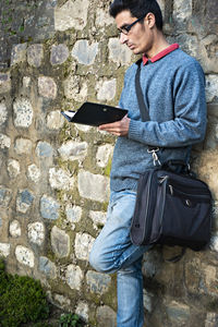 Man reading book while leaning on stone wall