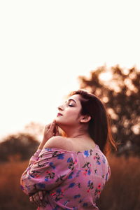 Young woman looking away while standing on land against sky during sunset