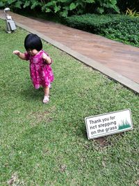 High angle view of girl walking by sign board on field at park