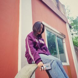 Side view of young man sitting against wall