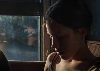 Close-up of young woman looking down near the window