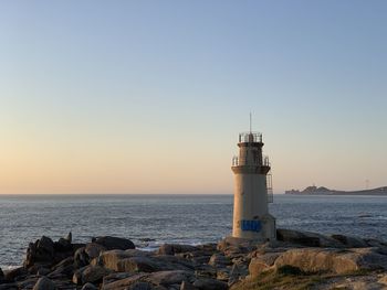 Lighthouse by sea against clear sky during sunset