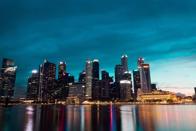 Illuminated buildings by bay against sky at night