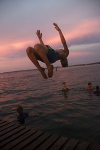 Men jumping on beach against sky during sunset