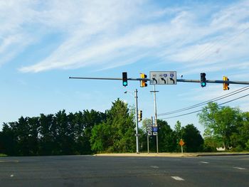 Illuminated stoplight with arrow symbols over empty road against blue sky