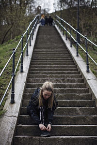 Full length of young woman tying shoelace on steps