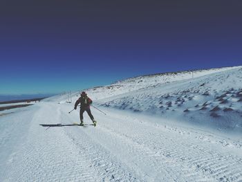 Rear view of man skiing on snowcapped mountain against clear sky