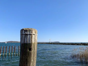 Wooden posts in sea against clear blue sky