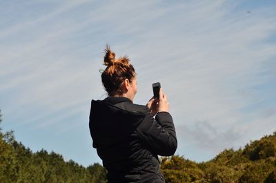 Man photographing with mobile phone against sky