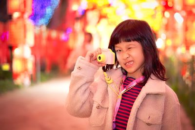 Portrait of cute girl photographing in illuminated carnival