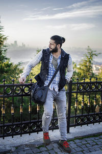 Full length of young man standing by railing against sky