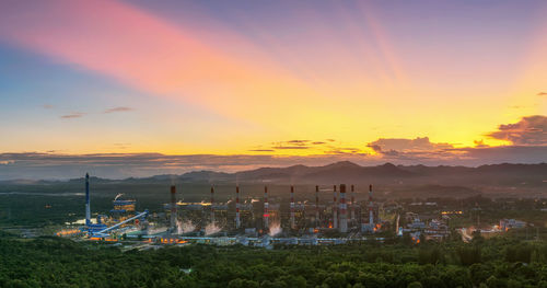 Factory and landscape against sky during sunset