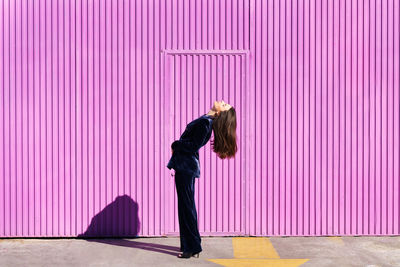 Side view of woman standing against pink wall
