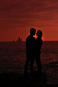 Silhouette of couple standing on sea at sunset