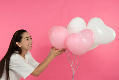 Woman holding balloons against pink background