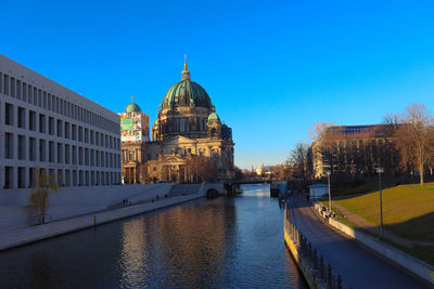 View of buildings by river against clear blue sky