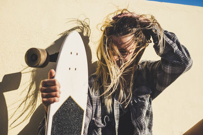 Portrait of smiling young woman holding surfboard against wall