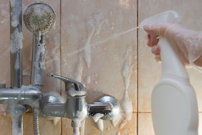 Midsection of person with faucet against wall in water