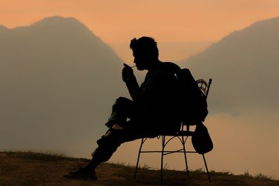 Silhouette man igniting cigarette against mountains during sunset